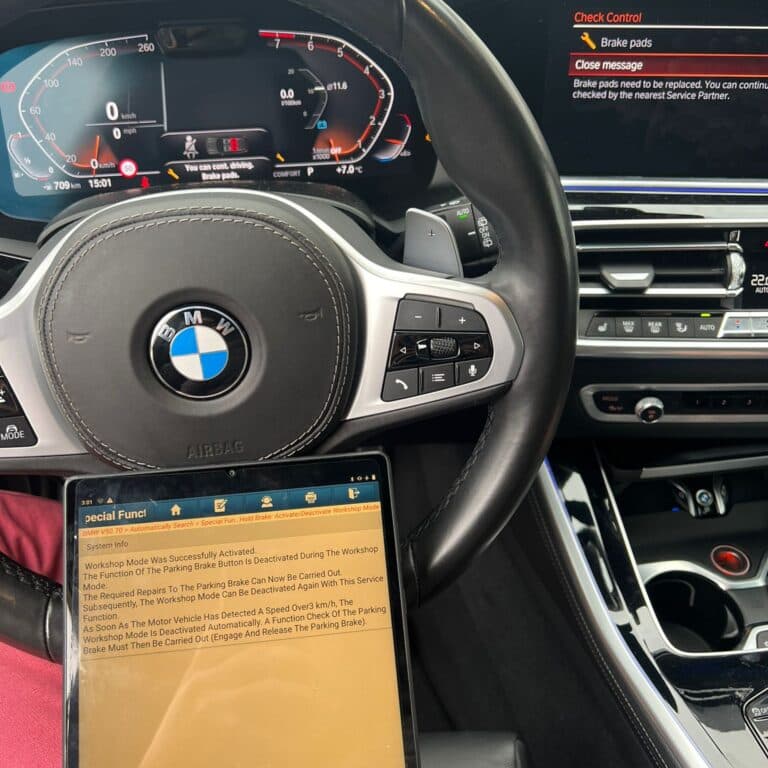 Interior BMW cu mesajul de uzură plăcuțe pe display, alături de tableta de diagnoză care activează modul service al frânei de mână electrice