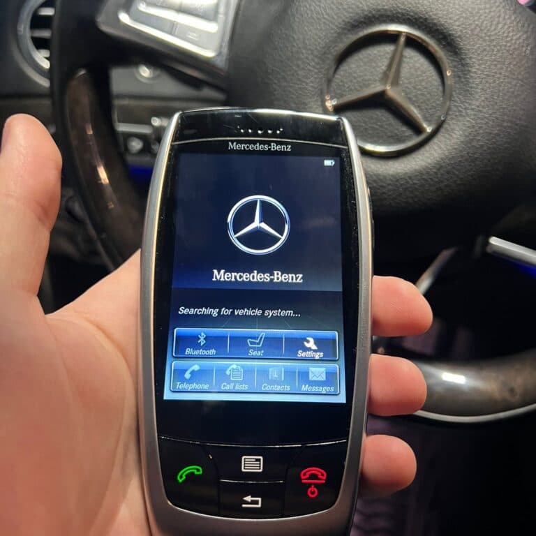 Cheie Mercedes-Benz cu display color, ținută în mână în fața volanului, în timp ce caută sistemul vehiculului