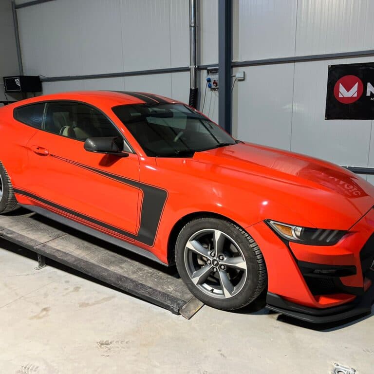 Ford Mustang roșu cu dungi negre, poziționat pe rulourile standului dyno din atelier