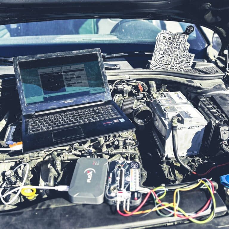 Compartiment motor deschis, cu laptop de diagnoză și programator FLEX conectate, iar mecatronicul cutiei automate așezat pe caroserie